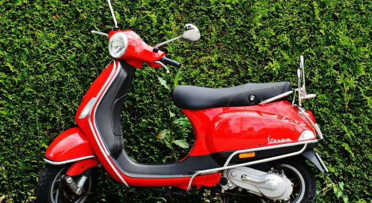 Scooter rouge devant une haie.